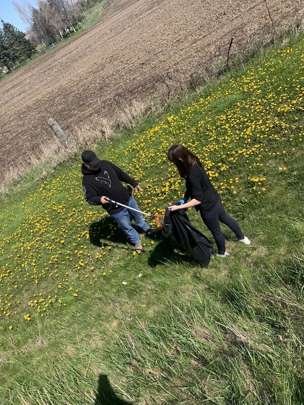 Two people picking up litter in a roadside field