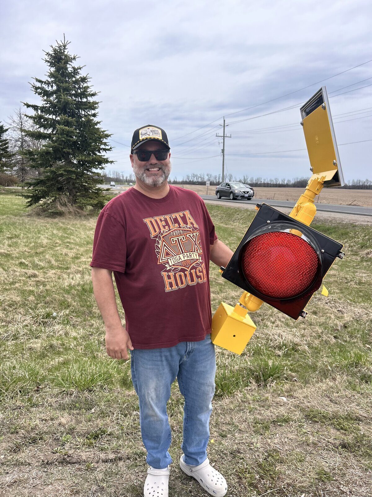 Fred Drodge holding a retired traffic signal head at a rural intersection